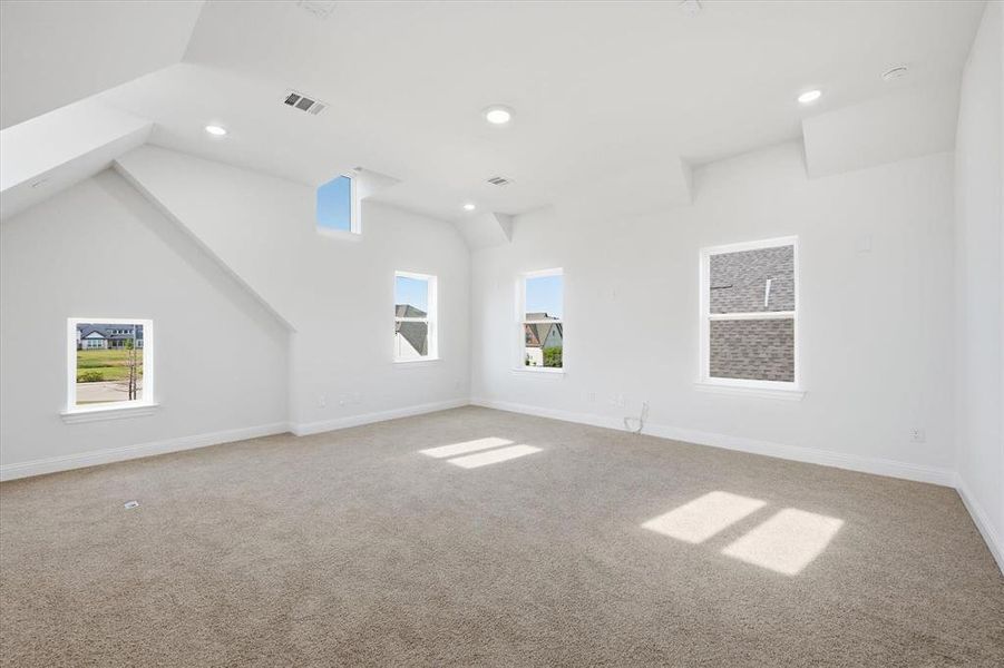 Spacious room featuring sloped ceilings, multiple windows, recessed lighting, and light-toned carpeting