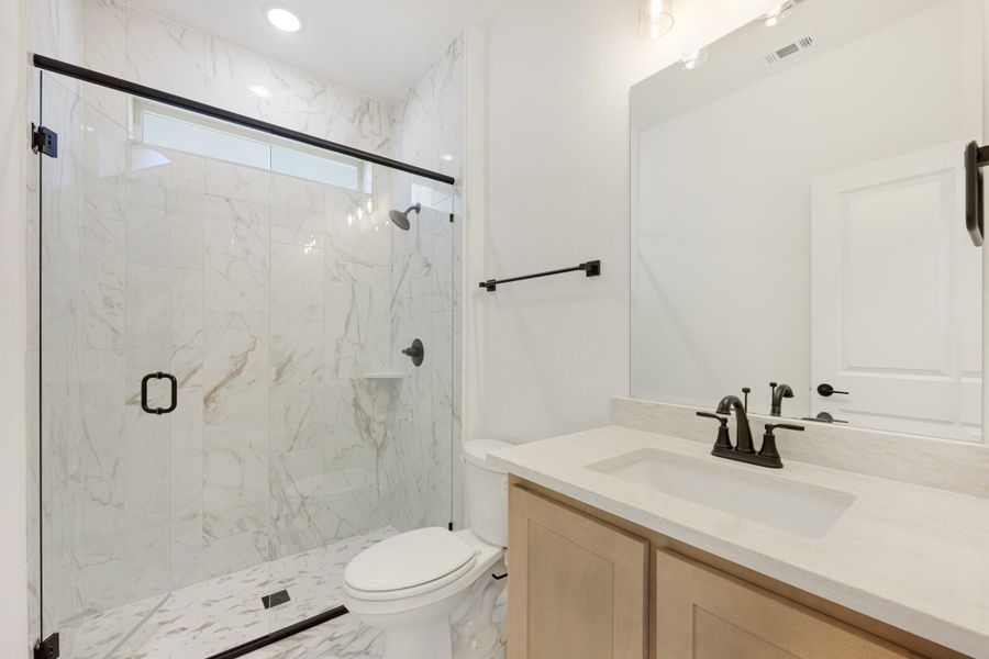 Bathroom with marble tile walk-in shower, glass door, wood vanity, and black fixtures