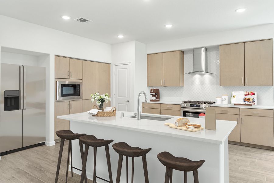 Kitchen with large white island, three bar stools, tan cabinets, and stainless steel appliances