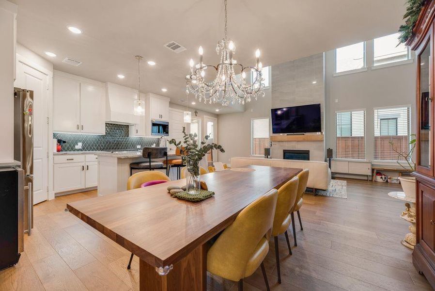 Dining area featuring light wood finished floors, suspended lighting, a fireplace, and a high ceiling