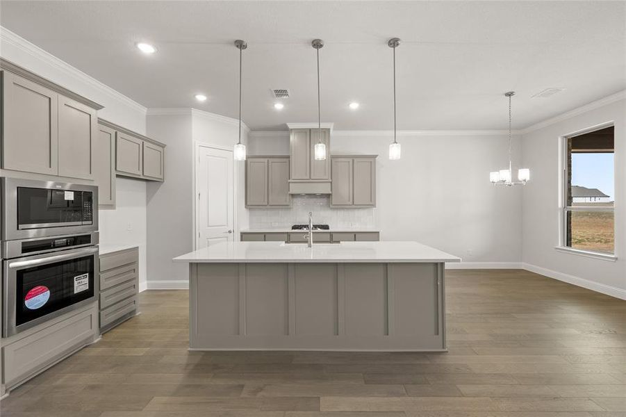 Kitchen featuring gray cabinets, stainless steel oven, built in microwave, backsplash, and light countertops Kitchen featuring gray cabinets, stainless steel oven, built in microwave, backsplash, and light countertops