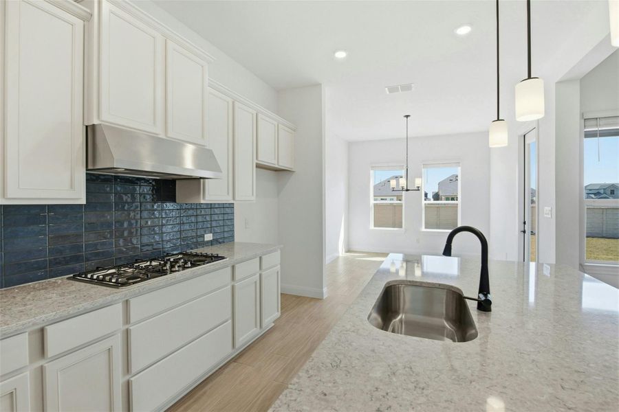 Kitchen with light stone counters, backsplash, light wood-type flooring, white cabinetry, and hanging lights