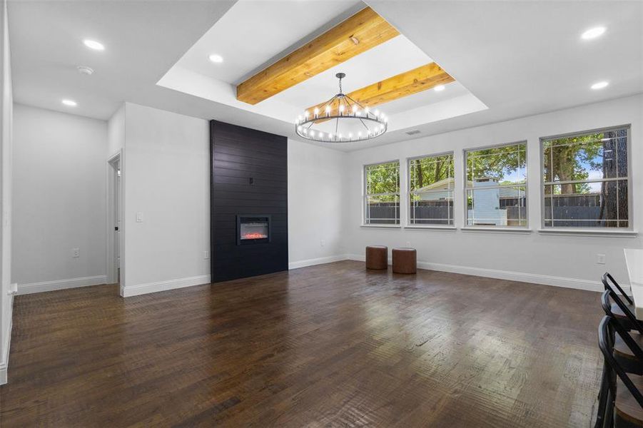 Unfurnished living room with recessed lighting, a chandelier, wood finished floors, a fireplace, and a raised ceiling Unfurnished living room with recessed lighting, a chandelier, wood finished floors, a fireplace, and a raised ceiling