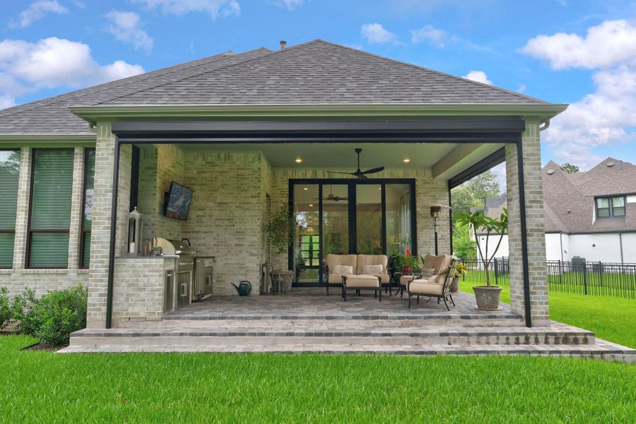 The covered outdoor living area is designed for true entertaining with a built-in kitchen, TV area, and upgraded wood ceiling. It extends the main living space outdoors and creates an inviting setting for year-round gatherings.