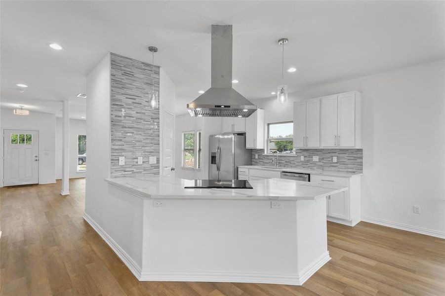 Spacious kitchen featuring a central island with a cooktop, quartz countertops, white cabinetry, and a stacked stone accent wall