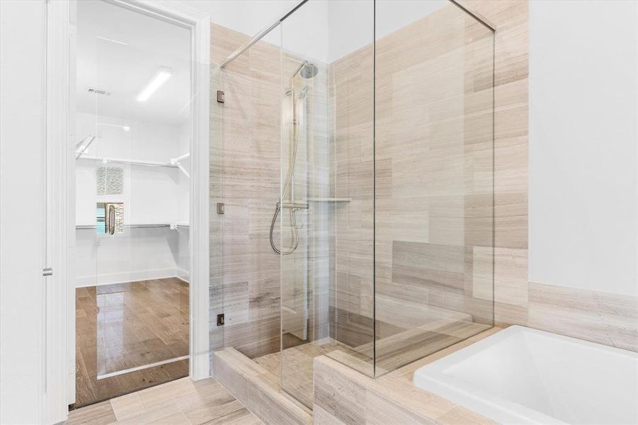 Full bath with a stall shower, a garden tub, a spacious closet, and light wood-type flooring Full bath with a stall shower, a garden tub, a spacious closet, and light wood-type flooring