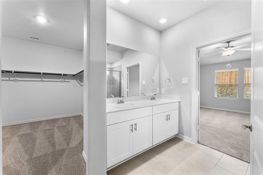 Full bathroom with double vanity, a spacious closet, a shower with door, a ceiling fan, and tile patterned flooring Full bathroom with double vanity, a spacious closet, a shower with door, a ceiling fan, and tile patterned flooring