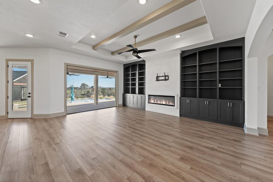 Unfurnished living room with light wood finished floors, visible vents, baseboards, a glass covered fireplace, and a ceiling fan