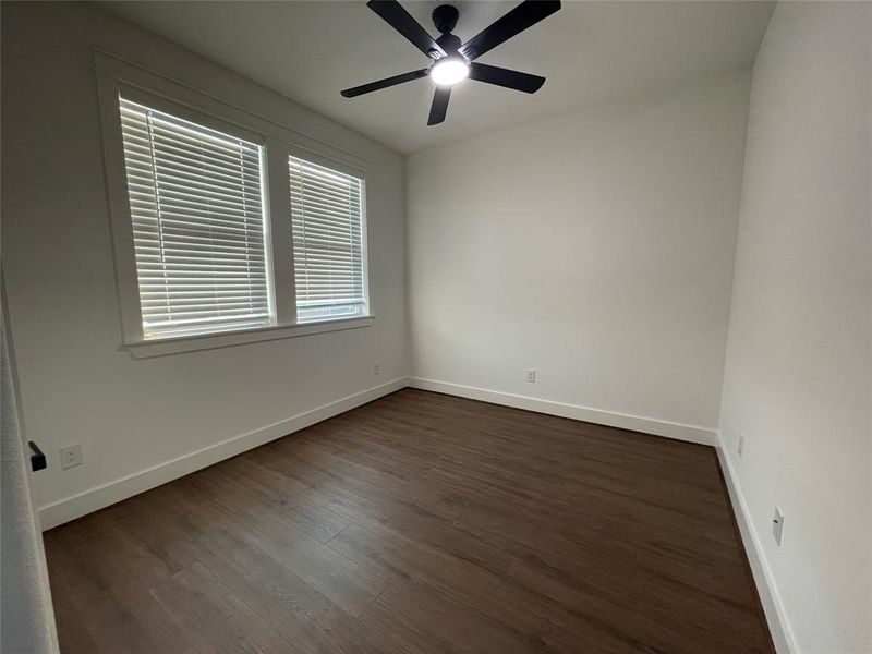 Empty room featuring dark wood-type flooring and a ceiling fan