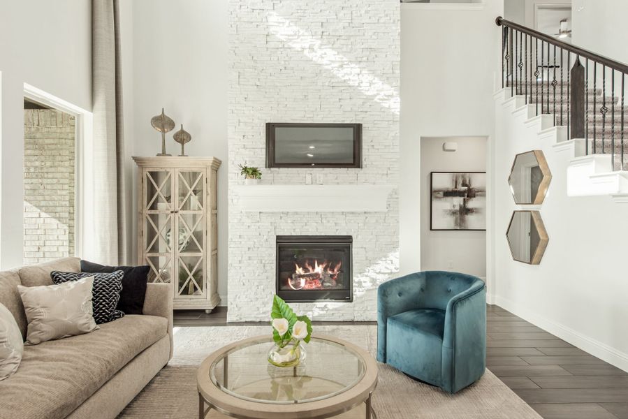 Living room with tall white stone fireplace, mounted TV, sofa, and teal accent chair on hardwood floors