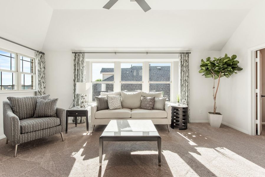 Bright living room with vaulted ceiling, ceiling fan, beige sofa, accent chair, and large windows with carpet flooring