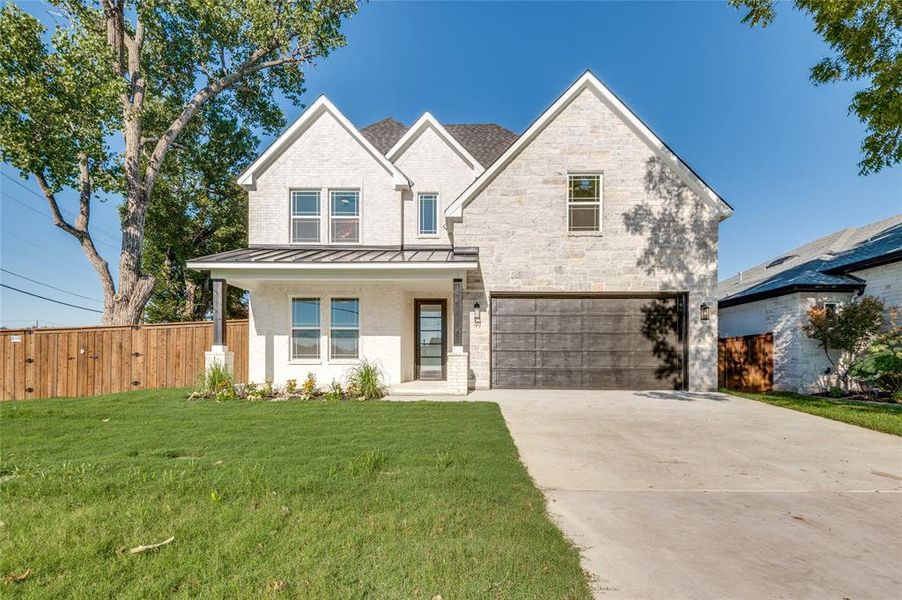 View of front facade with a standing seam roof, brick siding, a porch, driveway, and a garage