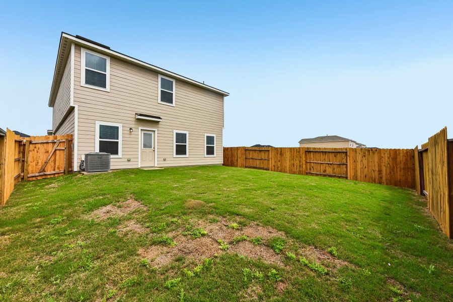 Spacious backyard featuring a full wood privacy fence, a manicured lawn, and a light-colored stucco exterior with multiple windows