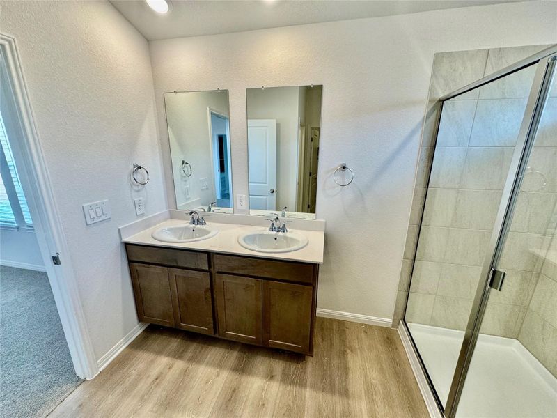 Full bath featuring a textured wall, a shower stall, light wood-style flooring, and double vanity Full bath featuring a textured wall, a shower stall, light wood-style flooring, and double vanity