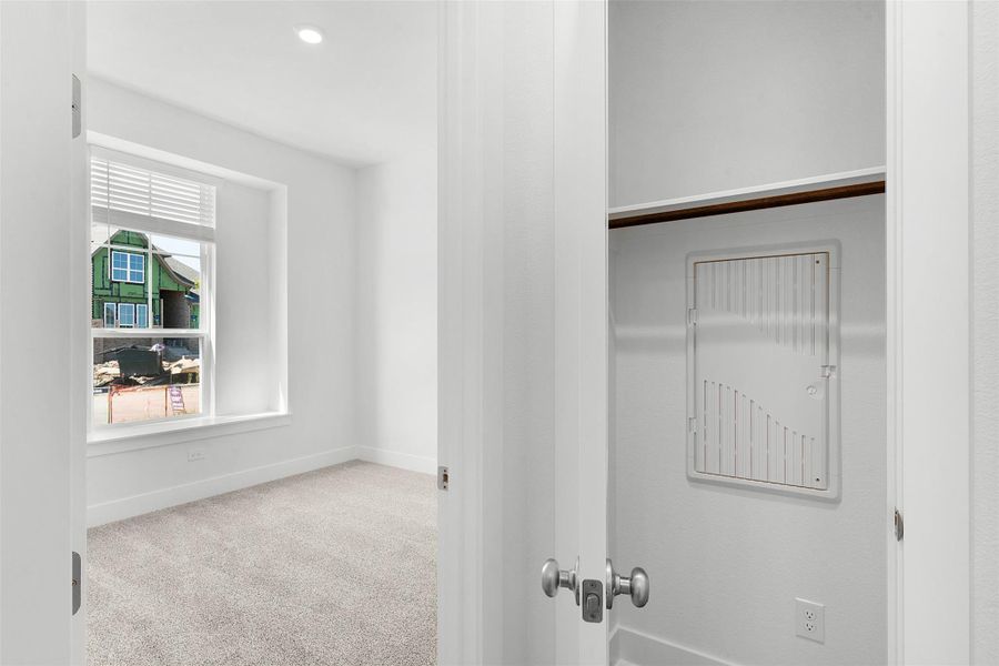 A well-lit bedroom features plush carpeting and a broad window.
