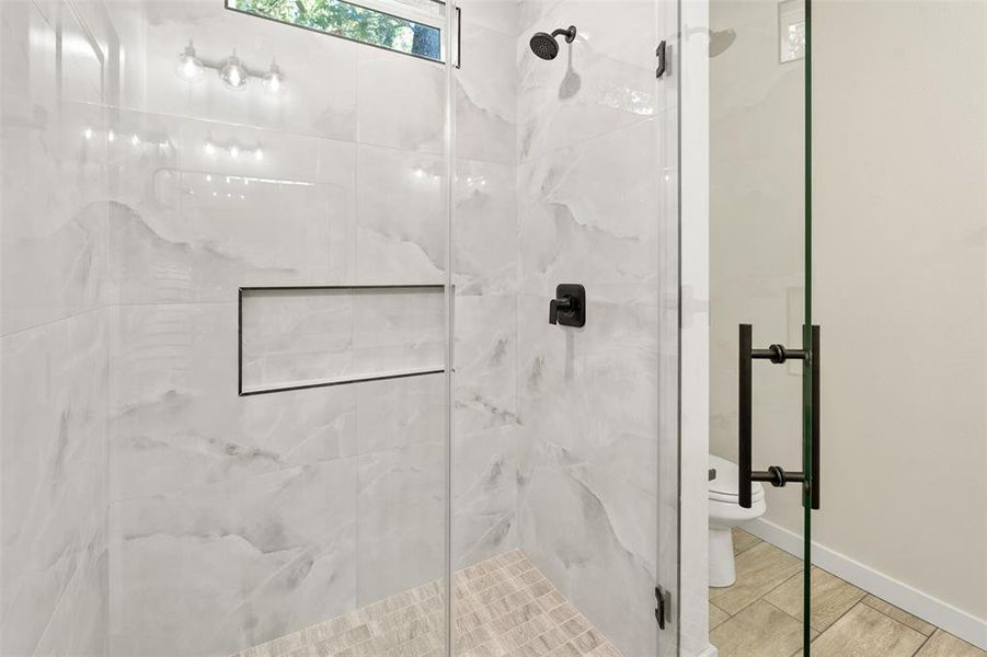 Glass-enclosed shower featuring large format white tiled walls with subtle veining, matte black shower fixtures, a recessed shower niche, and a mosaic tiled shower floor Glass-enclosed shower featuring large format white tiled walls with subtle veining, matte black shower fixtures, a recessed shower niche, and a mosaic tiled shower floor