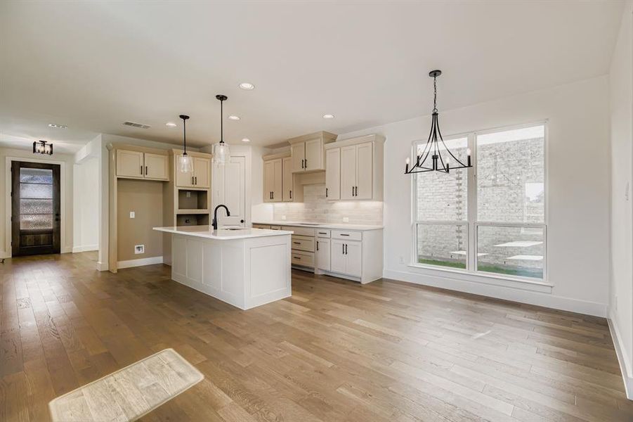 Kitchen with tasteful backsplash, a center island with sink, a chandelier, hanging light fixtures, and recessed lighting Kitchen with tasteful backsplash, a center island with sink, a chandelier, hanging light fixtures, and recessed lighting
