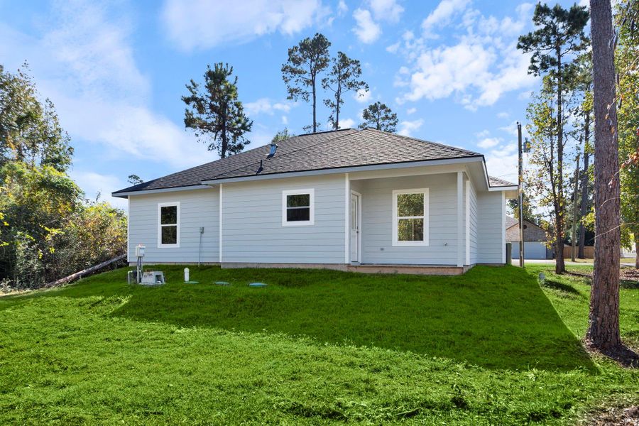 This photo showcases the rear exterior of the home, featuring a clean, modern look with light siding and white trim. The spacious yard offers plenty of open green space and backs up to a wooded area, adding extra privacy and a natural backdrop.
