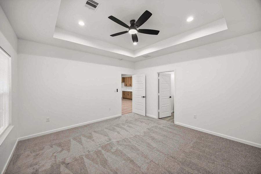 Spacious bedroom with plush carpeting, a modern ceiling fan, and elegant tray ceiling.