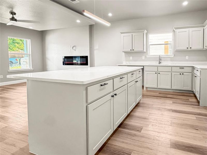 Spacious kitchen featuring a large island with white cabinetry, light countertops, wood-finish flooring, and an integrated fireplace