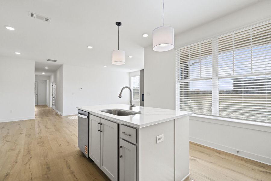 Kitchen with pendant lighting, gray cabinetry, light stone counters, an island with sink, and light wood-style floors