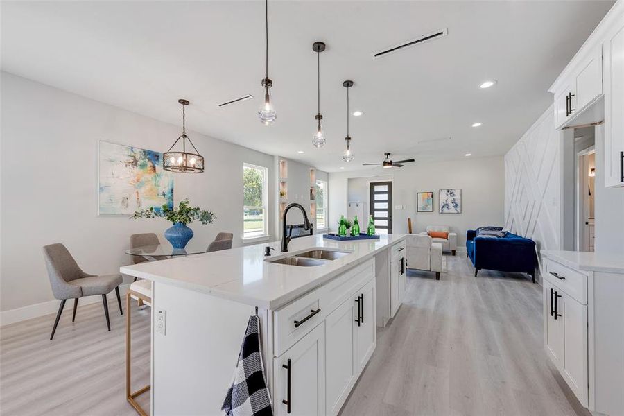 Kitchen featuring ceiling fan with notable chandelier, white cabinetry, sink, and an island with sink