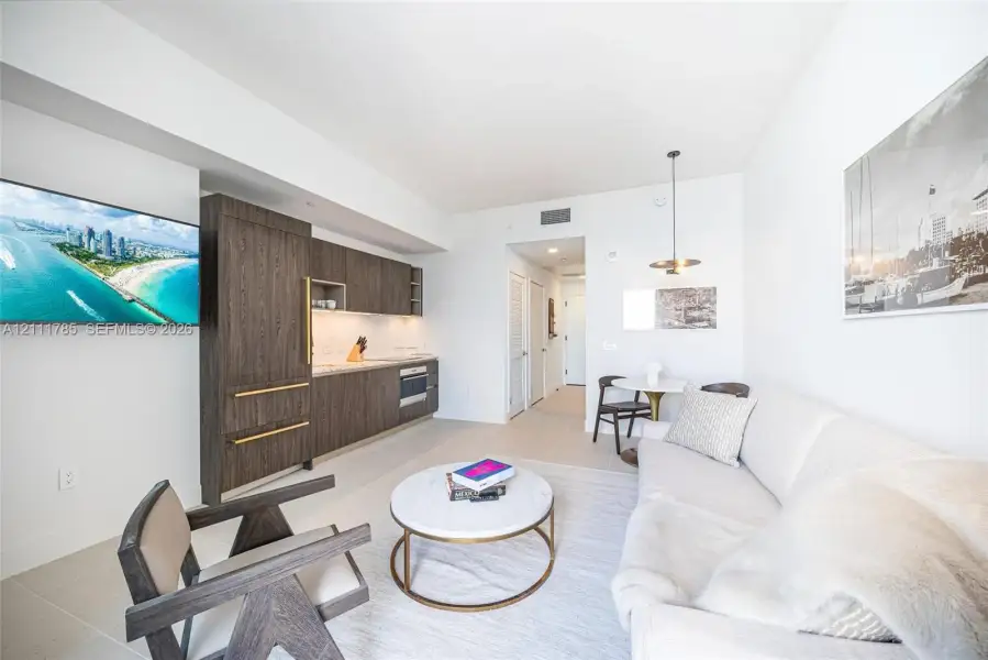 Kitchen featuring flat-panel wood-finish cabinetry, integrated appliances, and gold-tone hardware, complemented by neutral tile flooring and a minimalist pendant light fixture