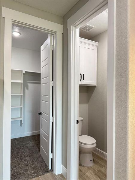 Powder room featuring a built-in white cabinet with black hardware, wood-finish flooring, and white trim