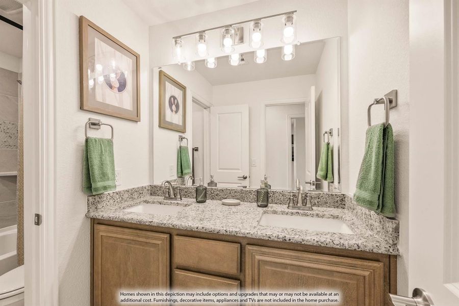 Bathroom with double sink vanity, granite countertop, wood cabinets, and large mirror with overhead lighting