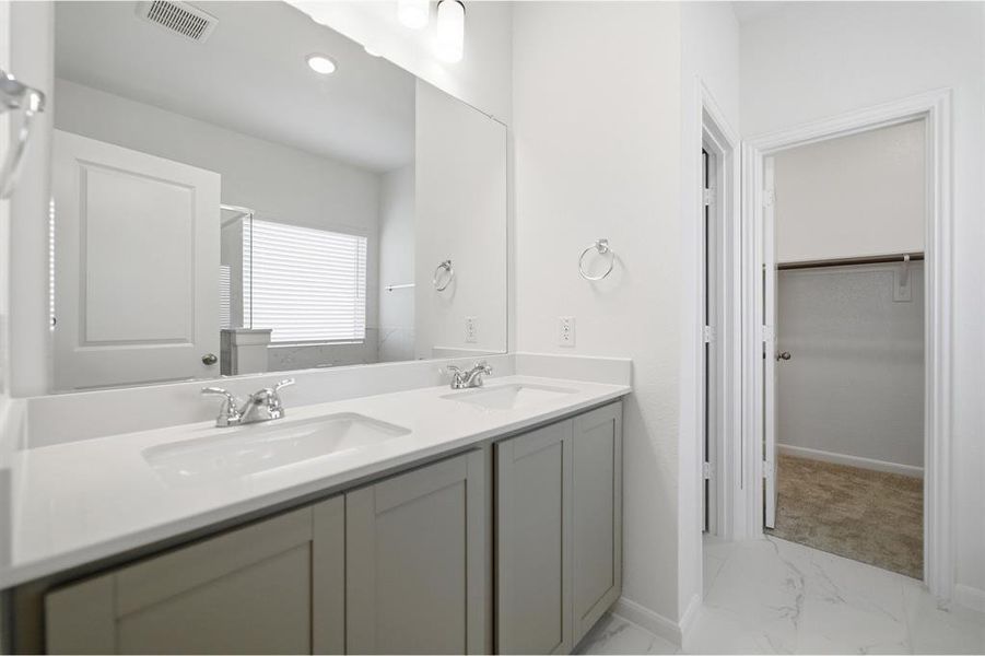 Bathroom with double vanity, light marble finish flooring, and a walk in closet