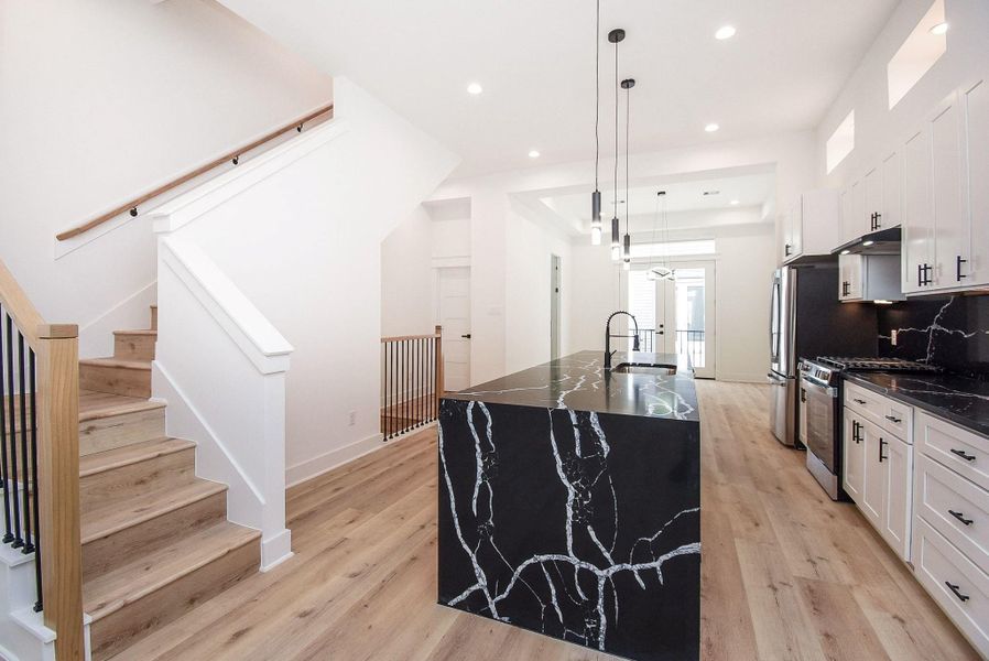 This modern kitchen features a striking black marble island with white veining, sleek cabinetry, stainless steel appliances, and light wood floors. The open layout is complemented by high ceilings and abundant natural light, creating a spacious and inviting atmosphere.
