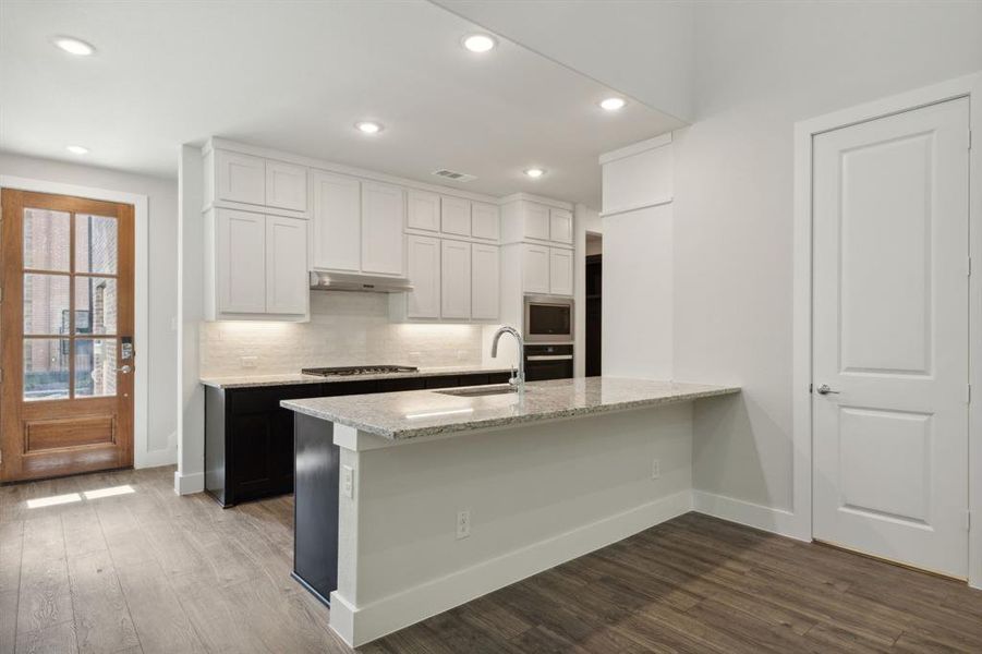 Kitchen featuring light stone counters, dark wood finished floors, backsplash, appliances with stainless steel finishes, and a sink