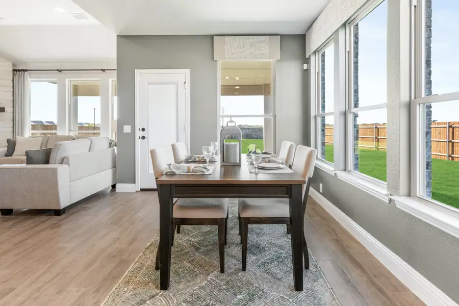 Dining area with dark wood table, four chairs, hardwood floors, and large windows overlooking a backyard