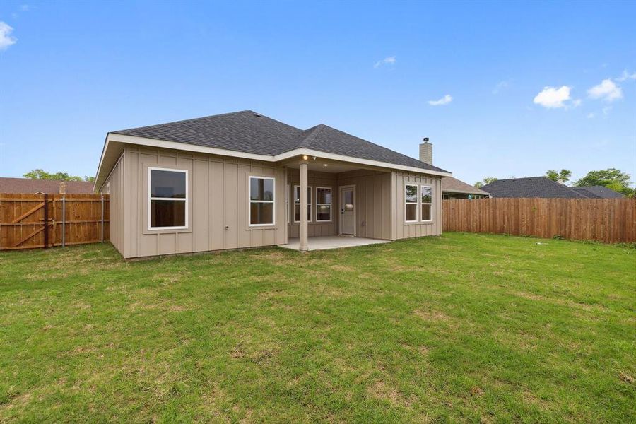 Rear view of property featuring a patio, a fenced backyard, board and batten siding, a shingled roof, and a yard