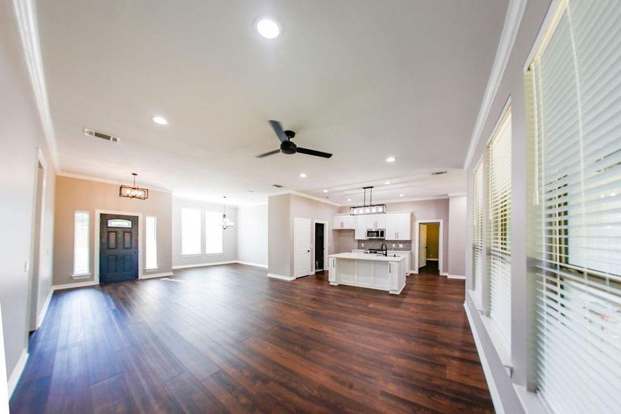 Unfurnished living room with crown molding, recessed lighting, dark wood-type flooring, ceiling fan, and a chandelier Unfurnished living room with crown molding, recessed lighting, dark wood-type flooring, ceiling fan, and a chandelier