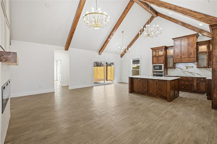 Kitchen featuring suspended lighting, glass insert cabinets, open floor plan, a center island with sink, and dark wood-style floors
