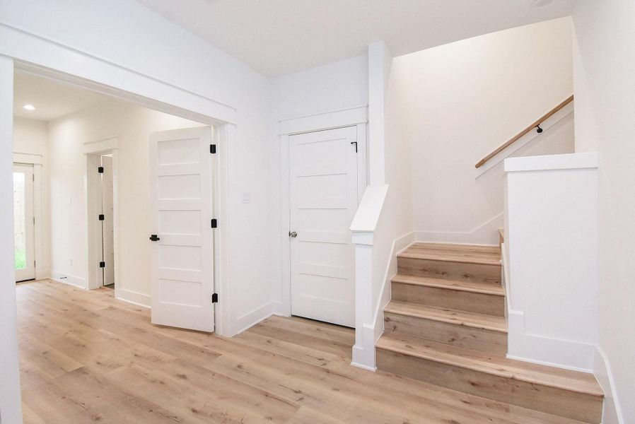 Bright and airy entryway with light wood flooring, white walls, and multiple doors. There's a staircase leading upwards, adding a modern touch to the home.