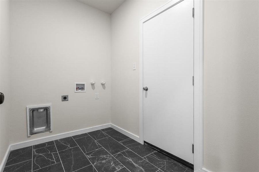 Dedicated utility space featuring dark, marbeled tile flooring, light-toned walls, and a white door with a silver knob