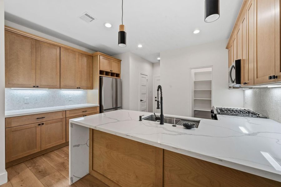 Modern kitchen featuring sleek quartz countertops, warm wood cabinetry, and stainless steel appliances, all enhanced by elegant pendant lighting and ample storage space.