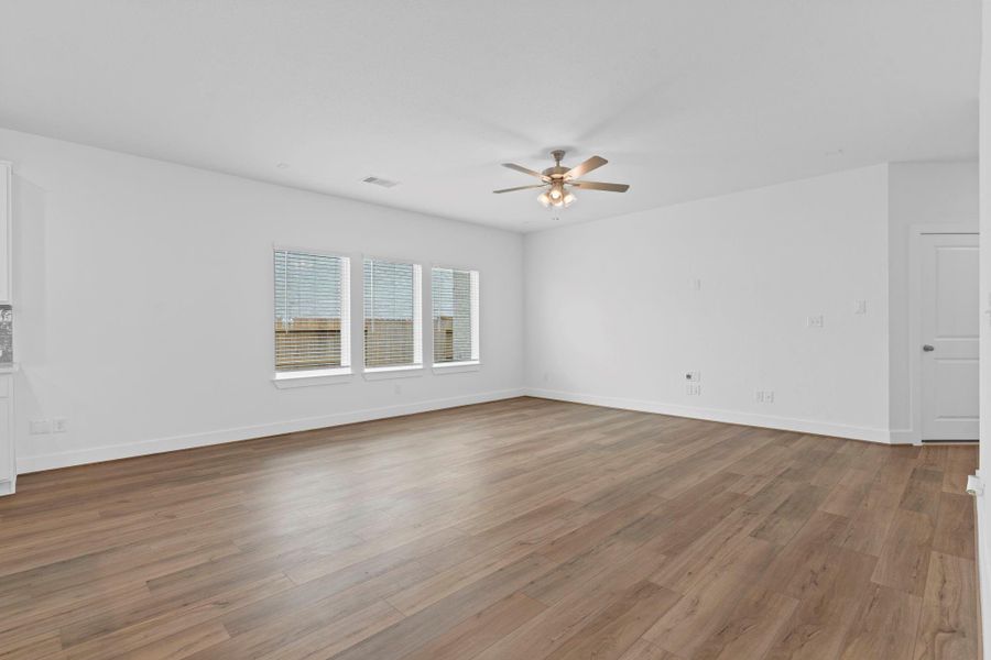 Spacious living area offers a flexible layout with rich wood-look vinyl flooring, a ceiling fan for comfort, and large windows that bring in natural light—perfect for cozy evenings or entertaining family and friends. **Image Representative of Plan Only and May Vary as Built**.