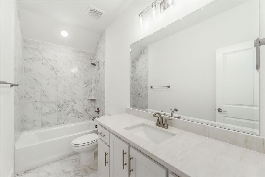 Bathroom with marble tile tub surround, white vanity with quartz countertop, and large mirror
