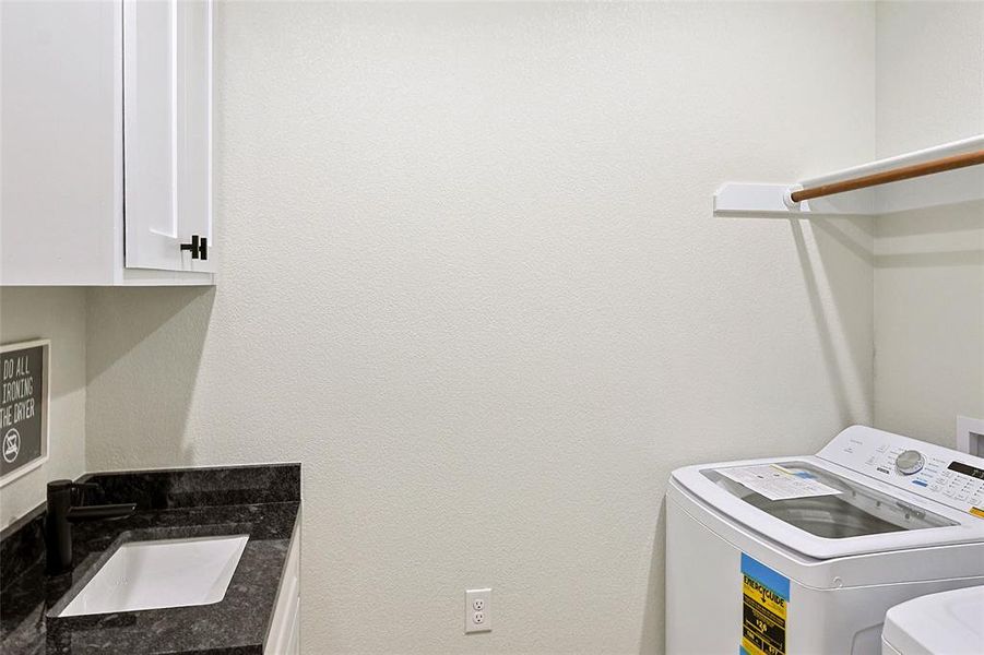 Laundry room featuring white cabinetry, a dark countertop with an undermount sink, a matte black faucet, and a wall-mounted hanging rod