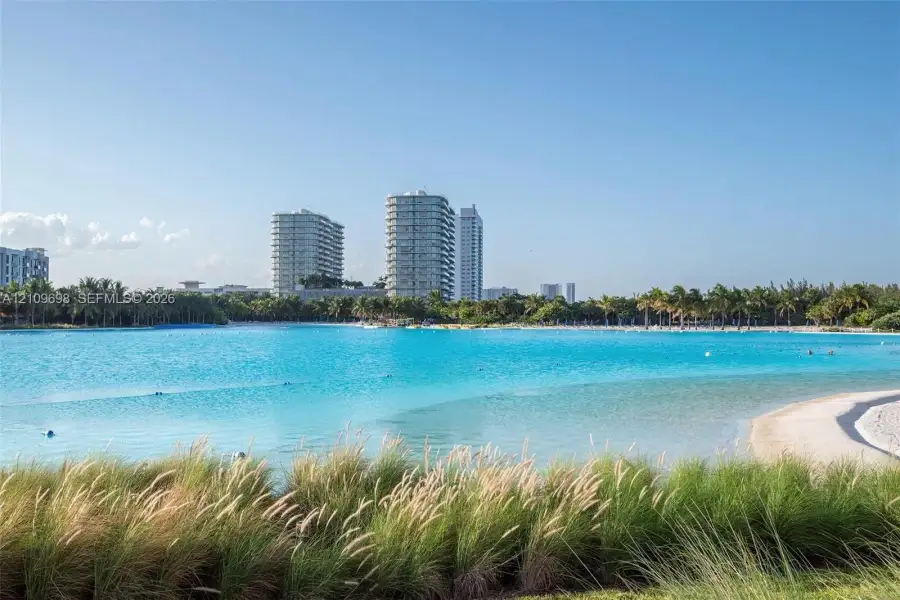 Expansive lagoon with a sandy beach shoreline, surrounded by tropical landscaping and mature palm trees