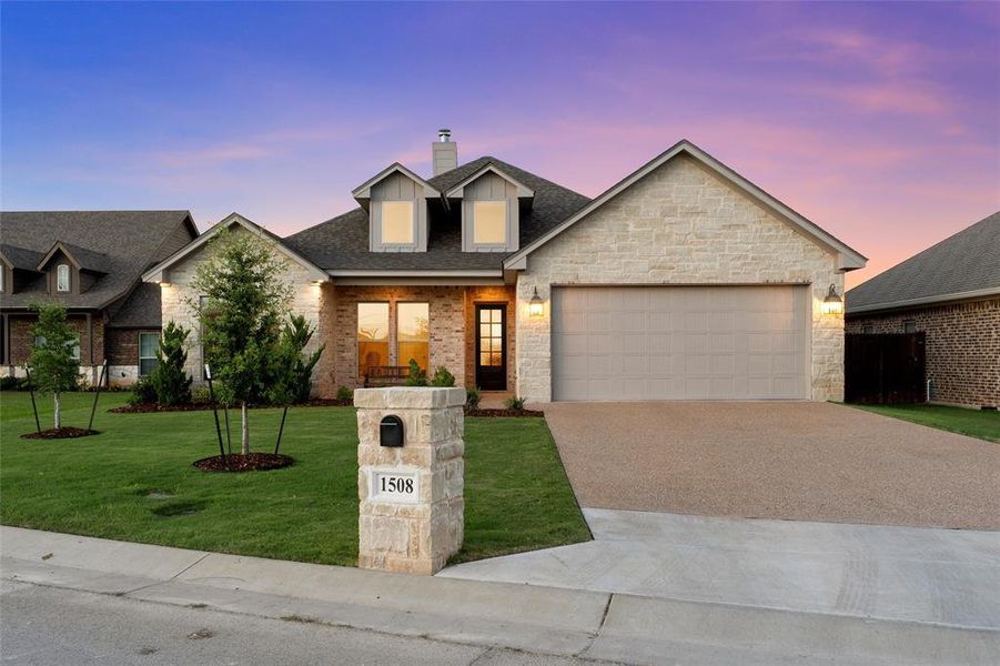 Stone and brick front elevation with two-car garage at dusk. Stone and brick front elevation with two-car garage at dusk.