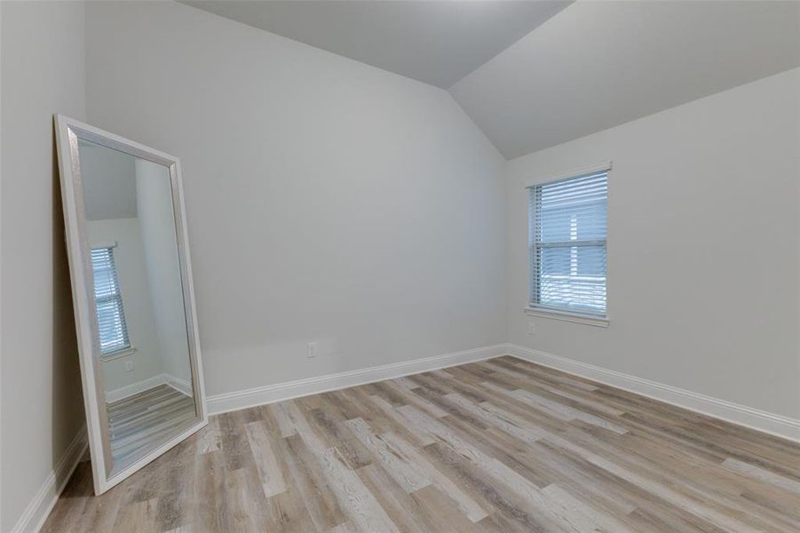 Empty room with light hardwood / wood-style floors and vaulted ceiling