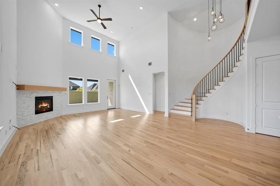 Unfurnished living room featuring light wood-style floors, stairs, a fireplace, a towering ceiling, and recessed lighting