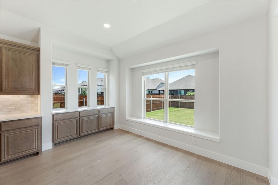 Dining area with light wood floors, brown cabinets, and large windows overlooking a backyard. Dining area with light wood floors, brown cabinets, and large windows overlooking a backyard.