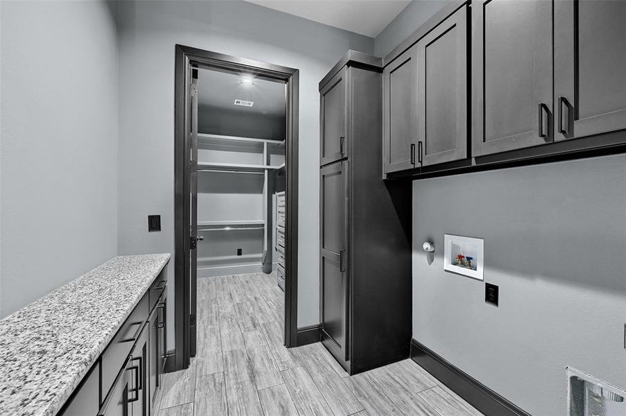 Laundry area featuring cabinet space, hookup for a washing machine, light wood-style flooring, and baseboards Laundry area featuring cabinet space, hookup for a washing machine, light wood-style flooring, and baseboards