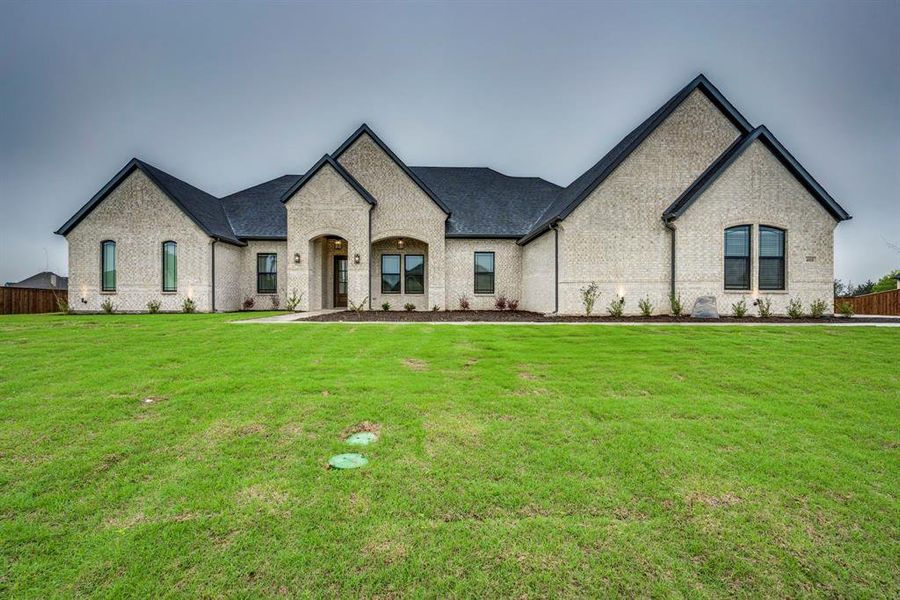 French country inspired facade featuring brick siding, a front lawn, fence, and roof with shingles