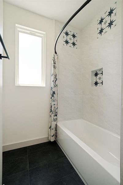 Bathtub and shower combination featuring white subway tile, stunning decorative accent tiles, a shower niche, and a black curved shower rod